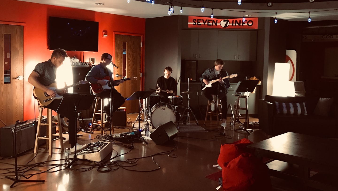Four musicians play instruments in a modern indoor music venue.