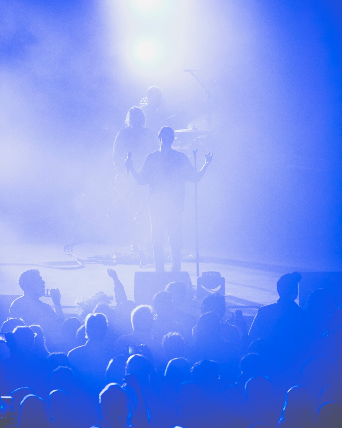 Lead singer on stage with arms raised to concert crowd.