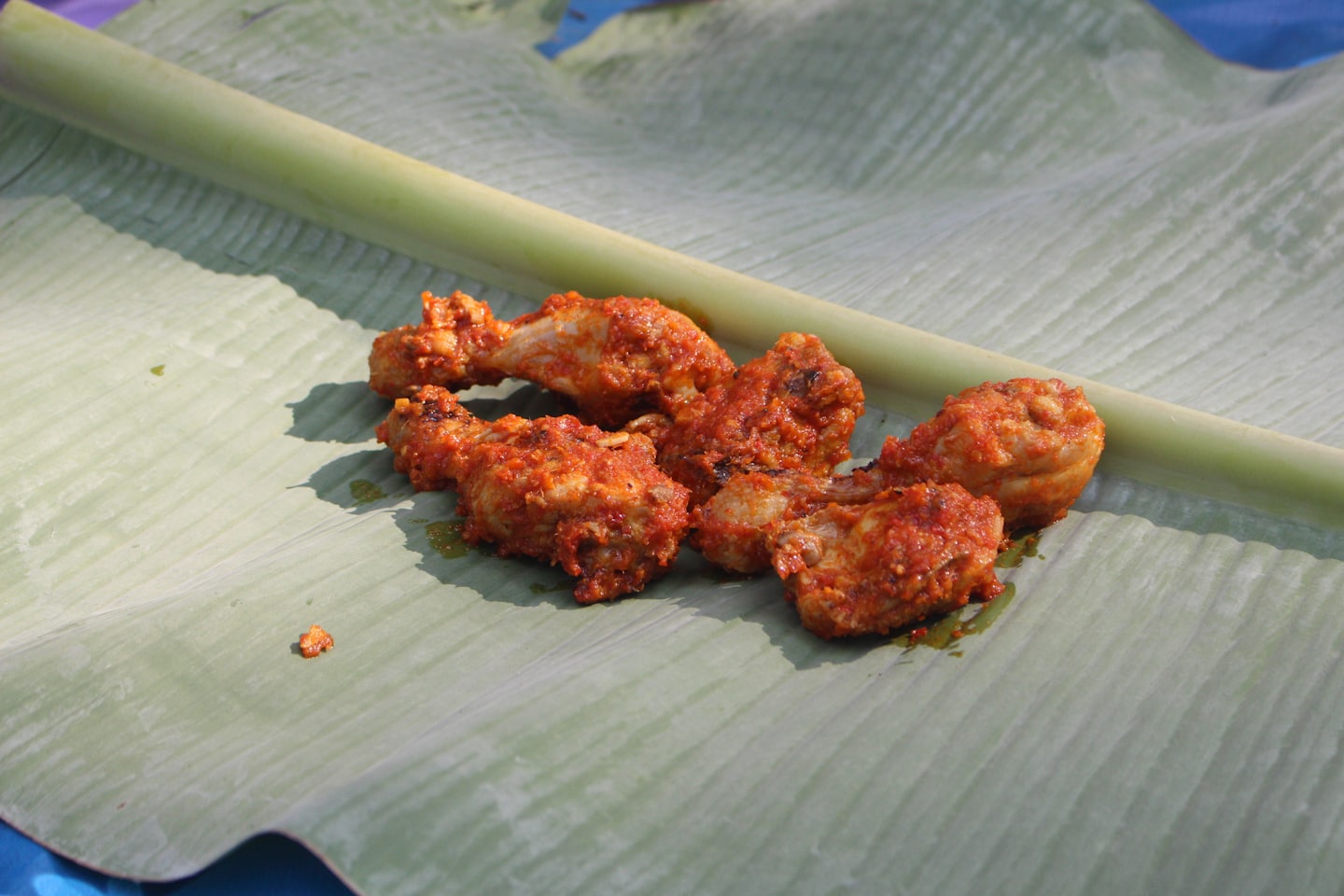 Spicy chicken drumsticks served on a large green banana leaf.