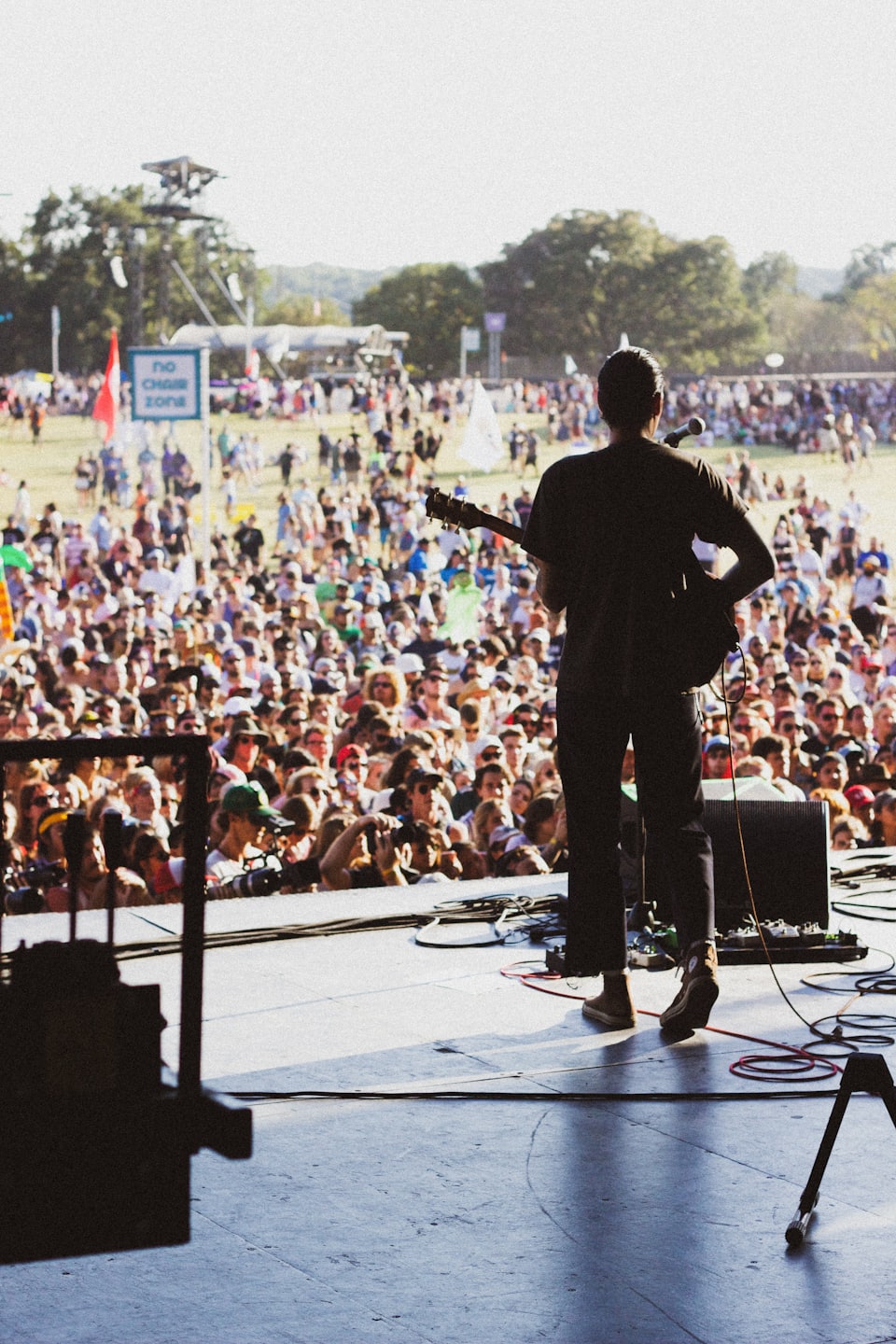 Musician plays guitar on stage at a sunny outdoor festival.