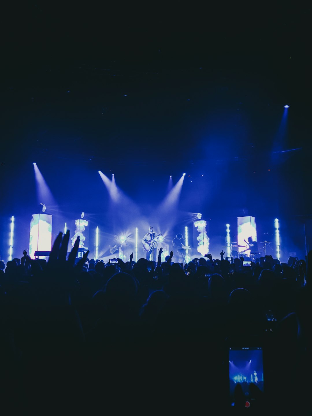 Band performs on stage before a cheering crowd with raised hands.