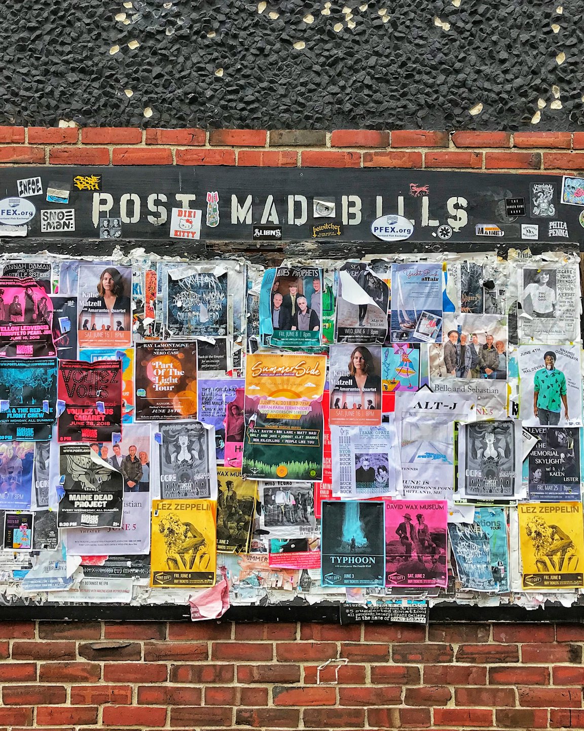 Concert and event posters layered on a brick bulletin board.